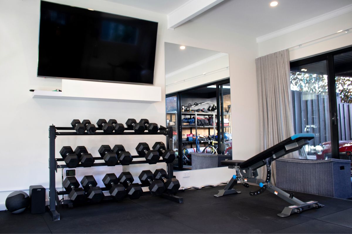 Private home gym with wall-mounted TV, mirror, dumbbell rack and adjustable bench